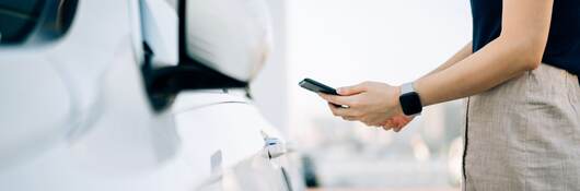 Close up of young Asian woman using mobile app device on smartphone to unlock the doors of her car in a car park.