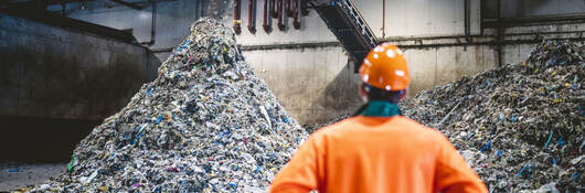 A worker wearing orange PPE and looking at recycling at a facility