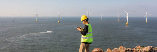Engineer reviewing data on the coast while overlooking a wind farm at sea