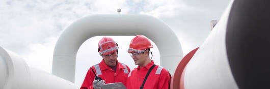 Two engineers having a discussion in front of pipes at a gas storage plant