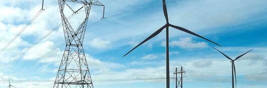 Wind turbines positioned on a plain next to electric grid towers