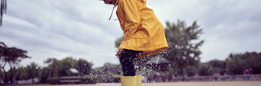 A child wearing rain gear and jumping in puddles
