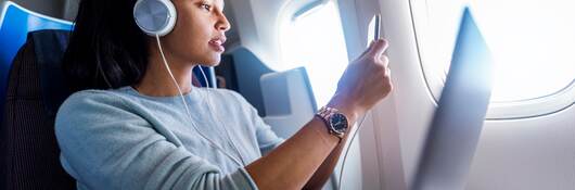 Person using mobile phone and laptop on a plane.