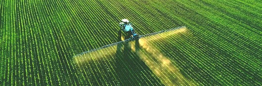 A tractor spraying fertilizer on a green field