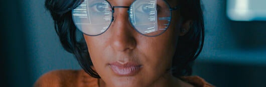 Person working on a computer with the screen reflecting in their glasses