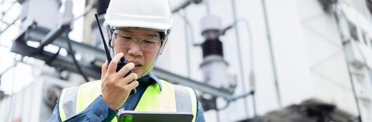 A worker wearing a hardhat and talking on a walkie talkie