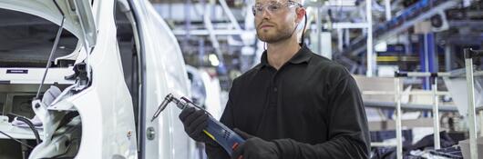 Engineer holding a drill while working on a production line in car factory
