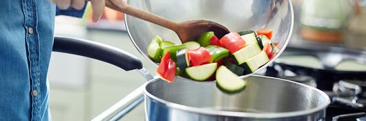 Person pouring cut vegetables into a pan on a gas stove.