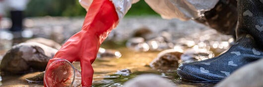 A person in PPE taking a water sample from a stream