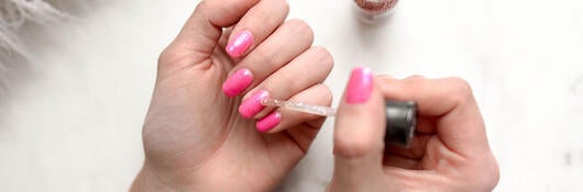 A person applying pink nail polish