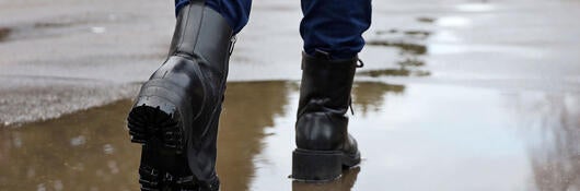 A person wearing boots and walking over a puddle