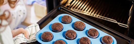 A person removing muffins baked in a silicone cupcake pan out of the over