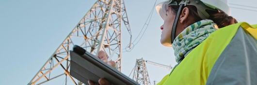 High voltage female engineer working in by a transmission tower