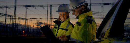Two engineers looking at reports near a power grid.