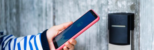 Woman in blue striped shirt holding a smart phone next to a digital lock