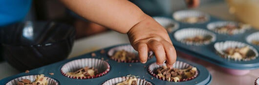 Small child reaching for an uncooked cupcake in a baking tray