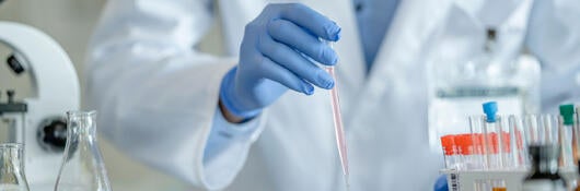 A laboratory technician dropping fluid into test tubes
