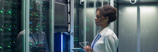 Technician working on a tablet in a data center full of rack servers running diagnostics and maintenance on the system.