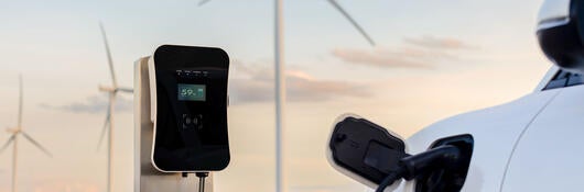 An EV charging at a charging station with wind turbines in the background