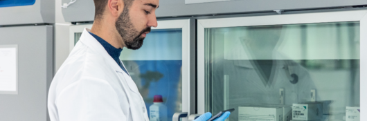 Scientist using a digital tablet near a laboratory refrigerator storing medical samples