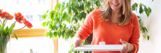 Woman in orange sweater opening a boxed package on a table