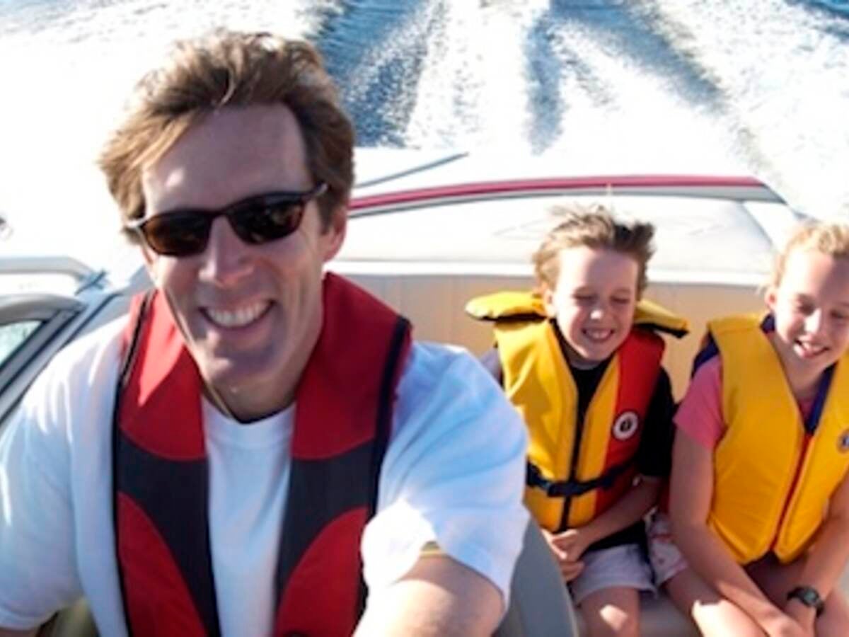 Family of three smiling, boating and wearing life jackets.