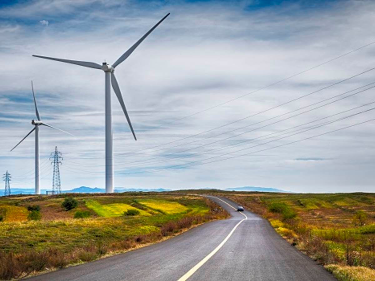 A wind turbine set to the left of a rural expressway.