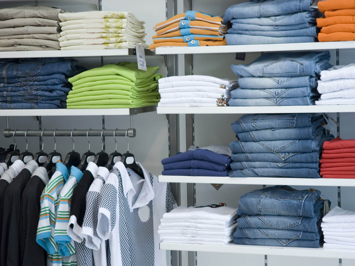 Retail store shelves filled with neatly folded clothes arranged by color. 