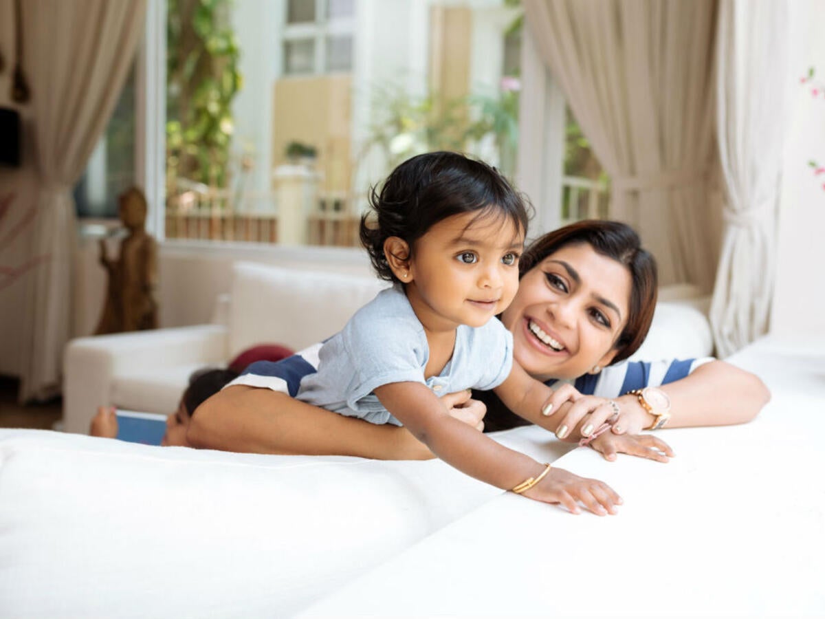 A smiling mother and child sitting on a couch while looking out the window. 