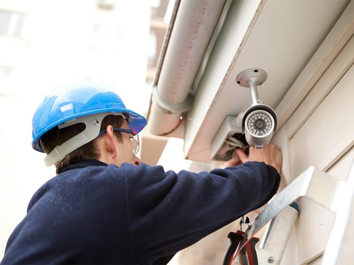 Man in hard hat on a ladder installing an outdoor security camera