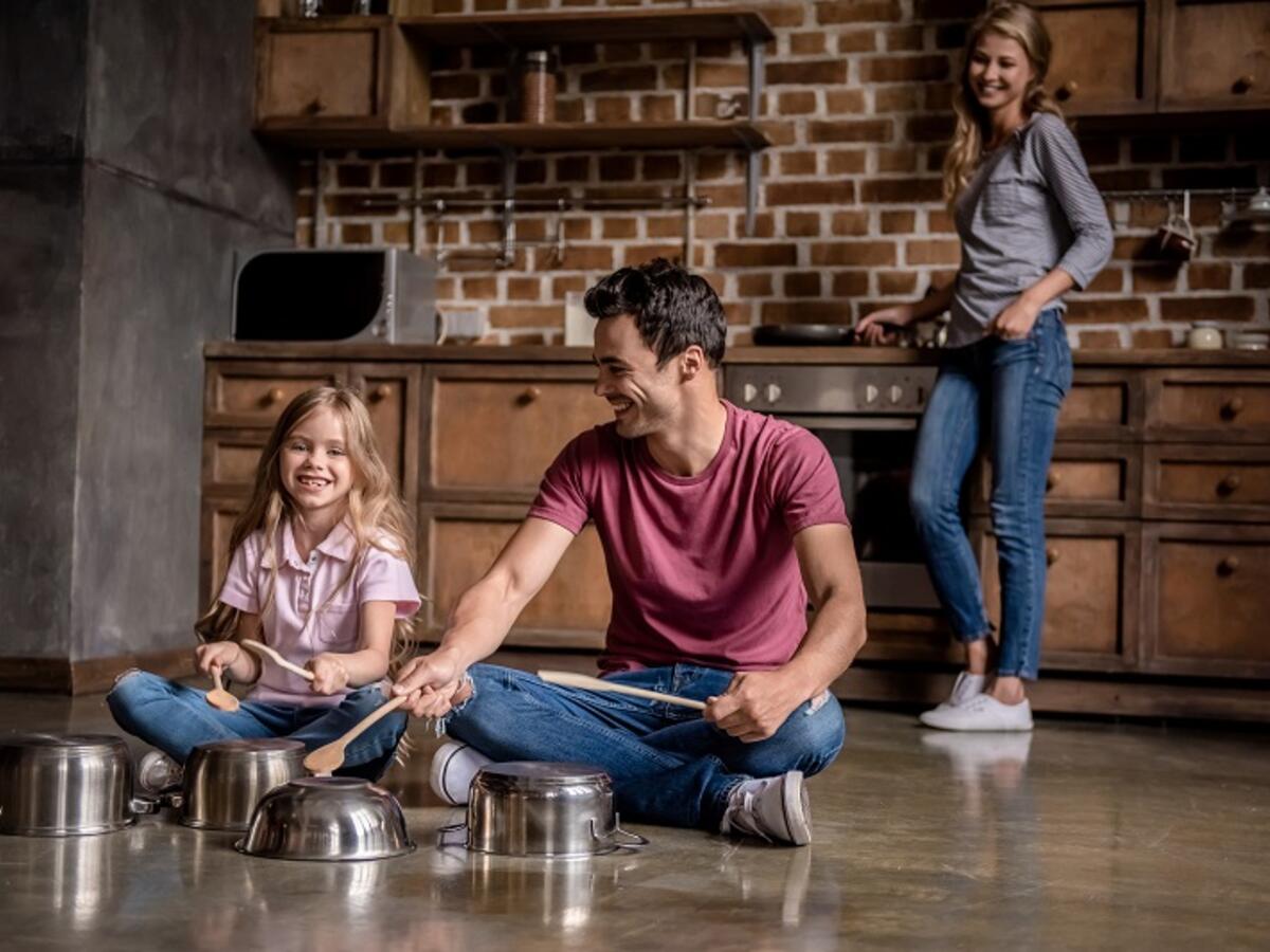 Father and daughter playing percussion on kitchen pots while mother watches from the stove