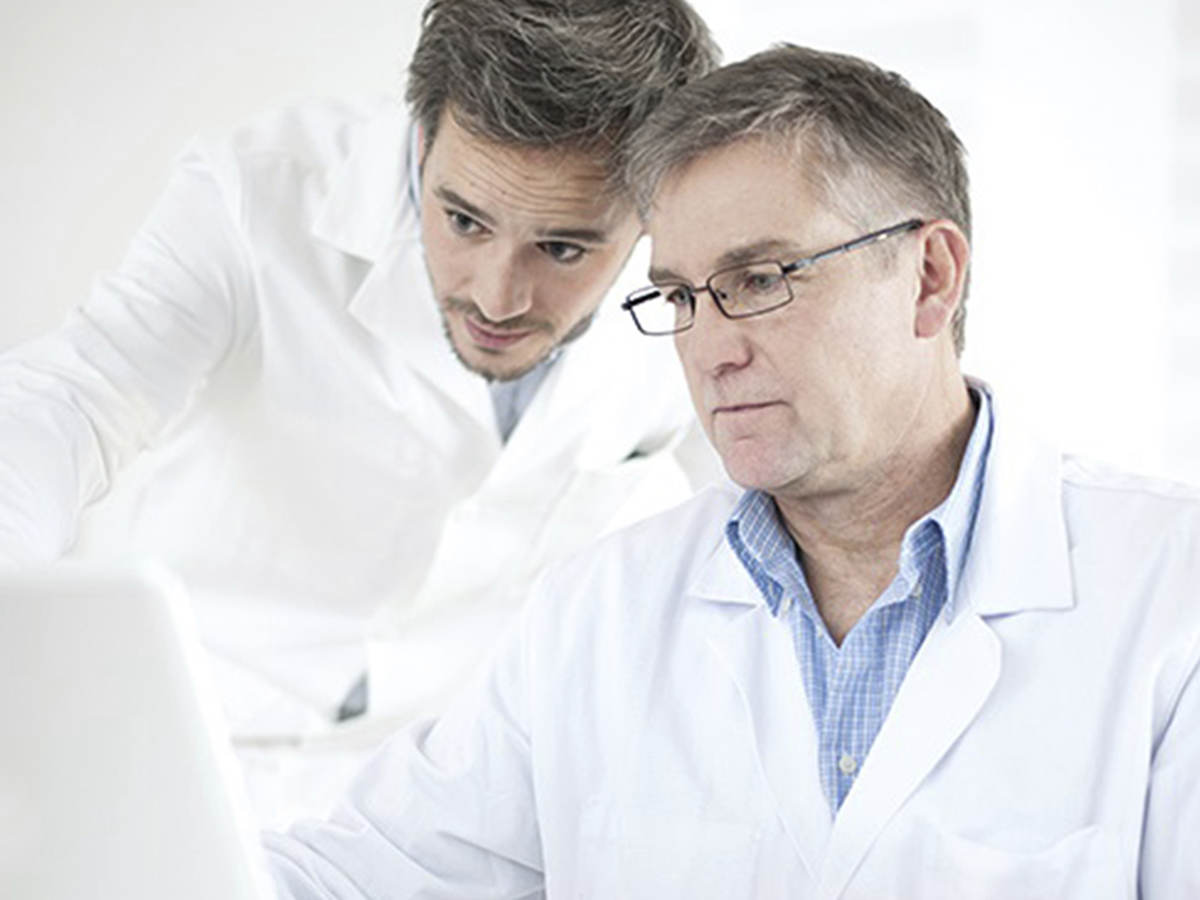 Two men in lab coats looking at a laptop. 
