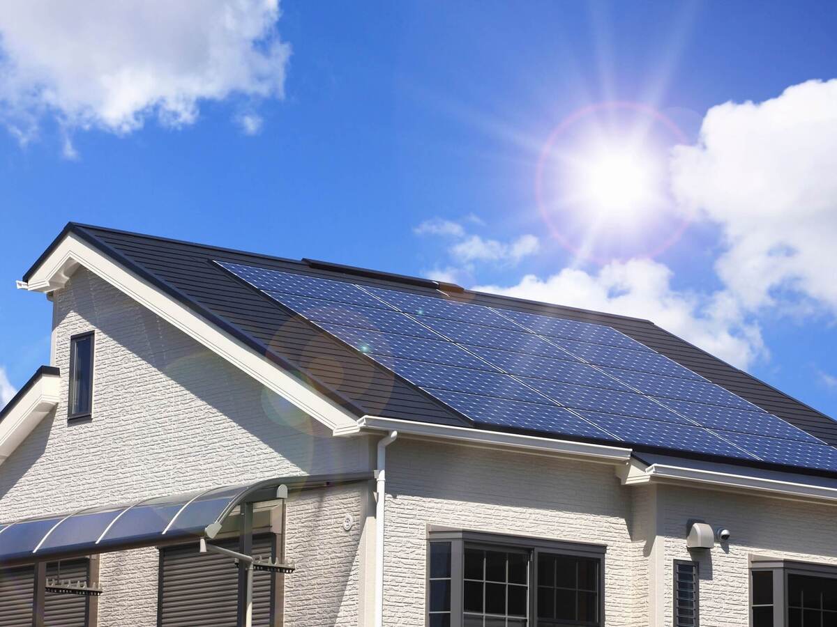 The sun shines brightly on the solar panels installed on the roof of a white, stucco home.