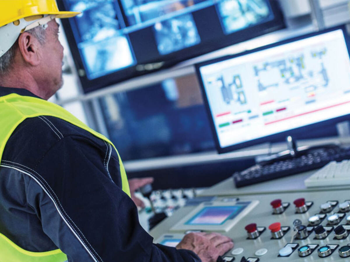 factory worker at a control panel pressing and looking at a monitor