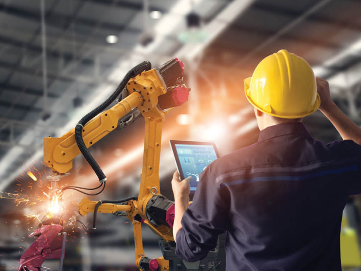 engineer in factory with tablet looking at robot arm