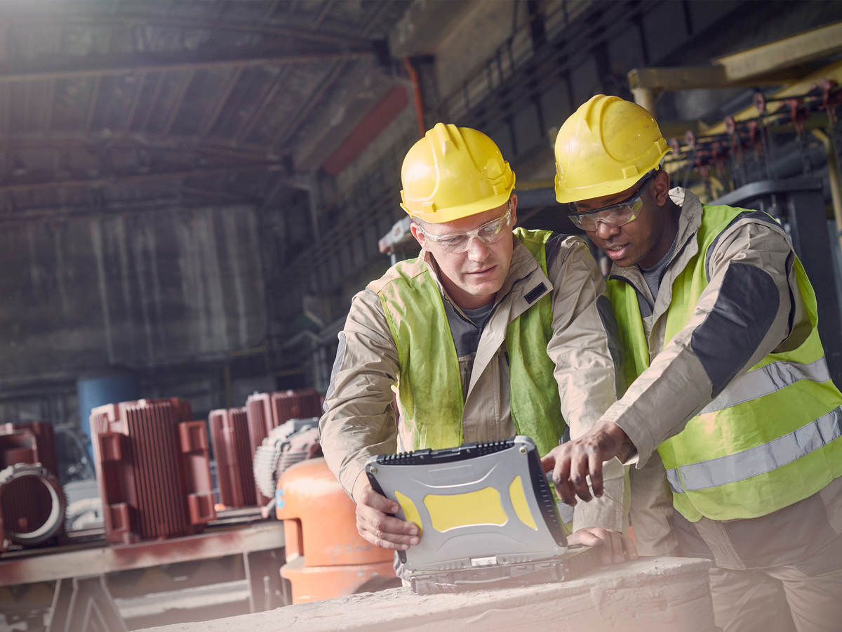 two men in protective gear look at a laptop