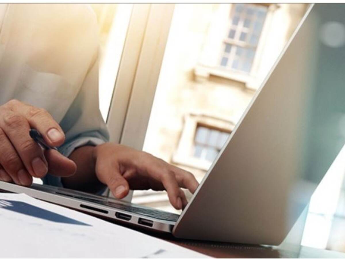 Hands typing on a laptop with windows in the background