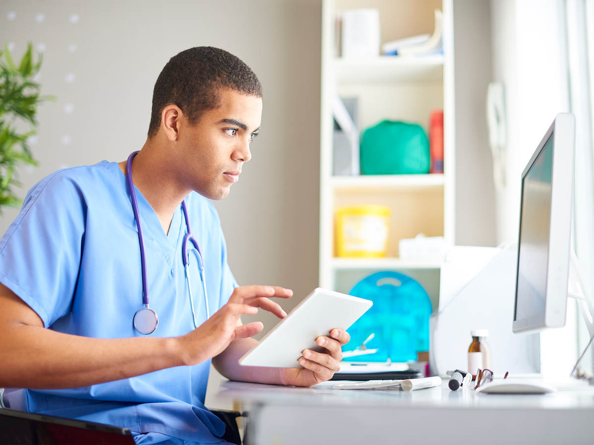 A medical professional reading a chart on a tablet and desktop monitor