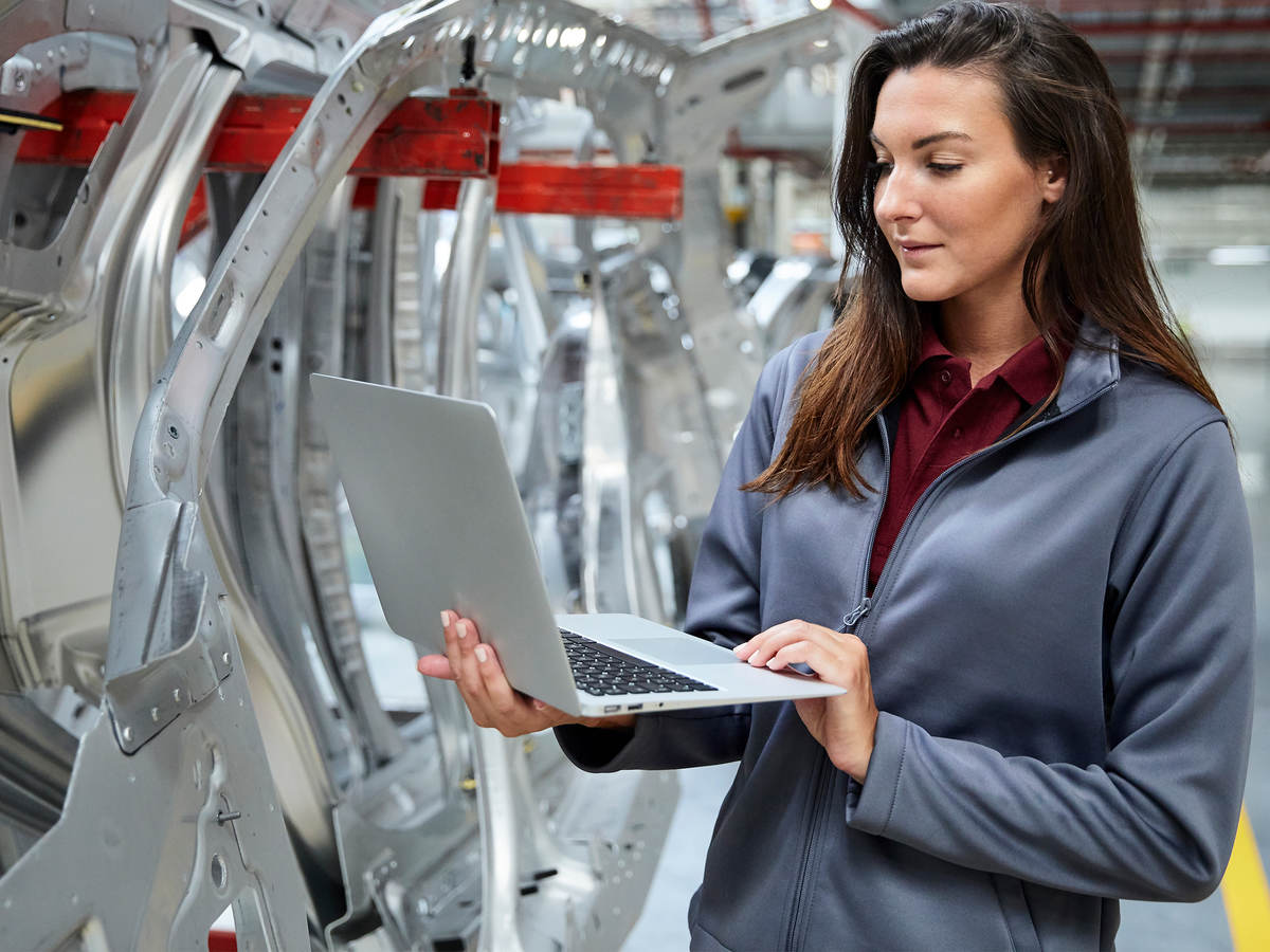 Woman with a laptop inspecting an automotive factory.