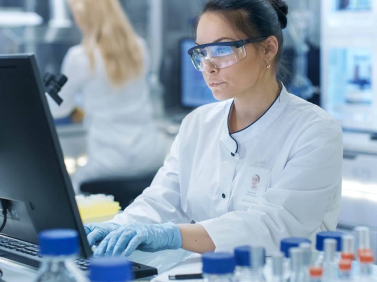 A scientist in a lab setting typing on a computer. 