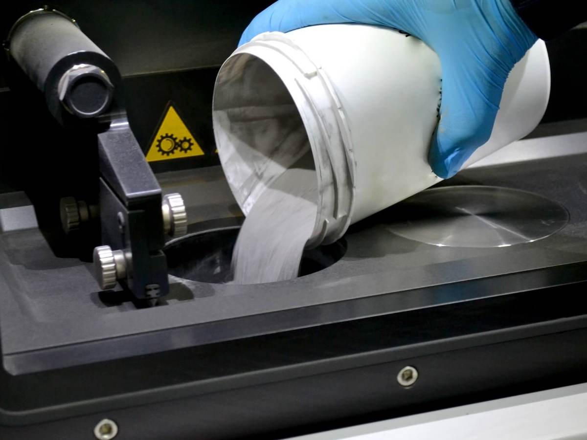 Man pours metal powder into the chamber of a laser sintering machine. 