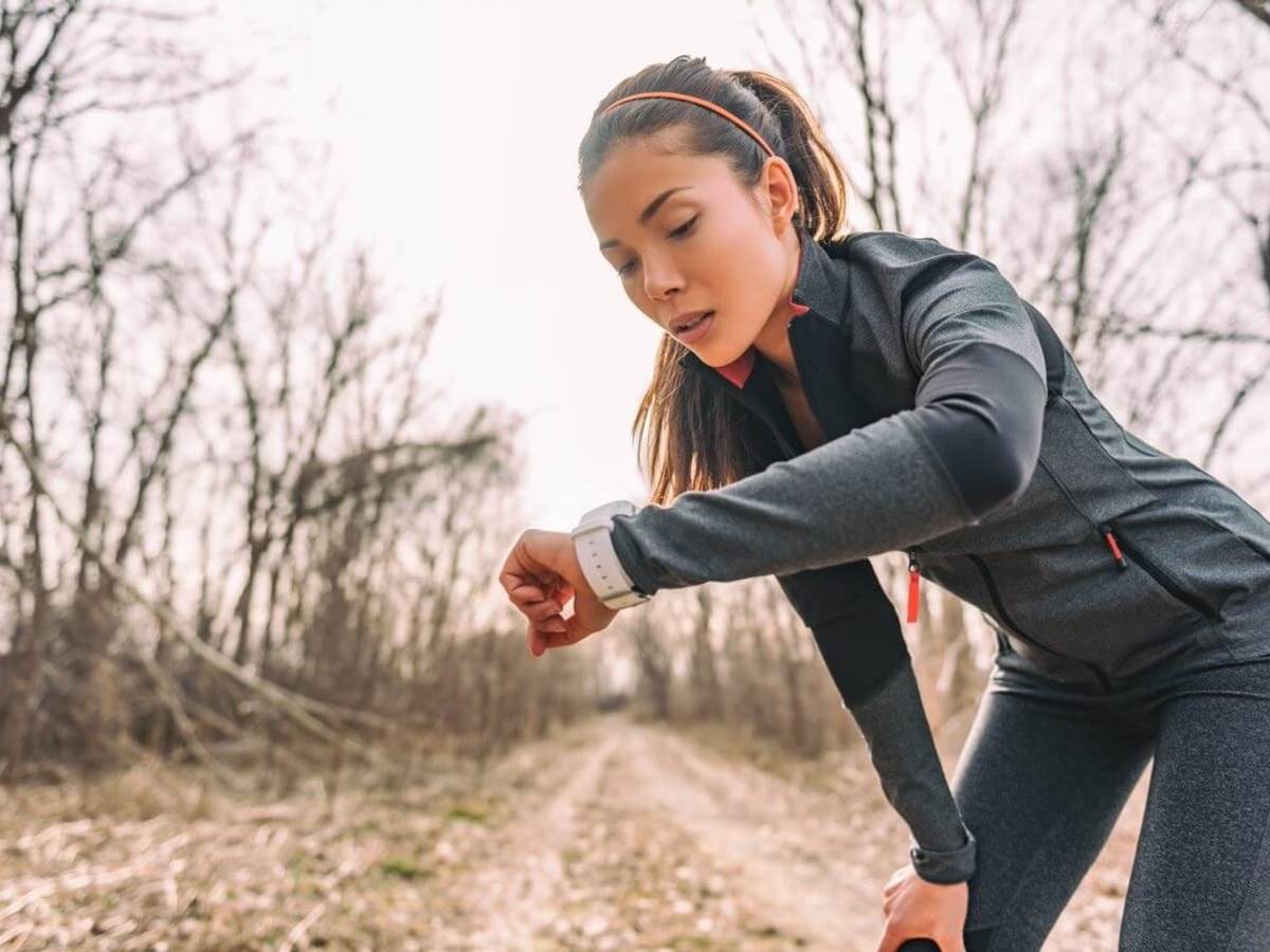 A female runner checks her time on her smart watch. She's wearing black on black performance material workout gear.