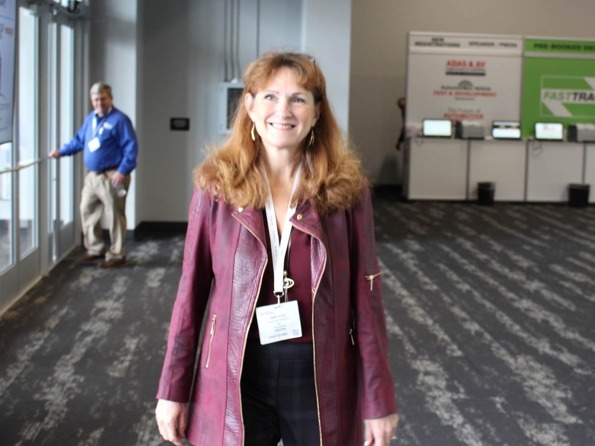 Woman wearing a burgundy jacket with black pants walks around event showroom