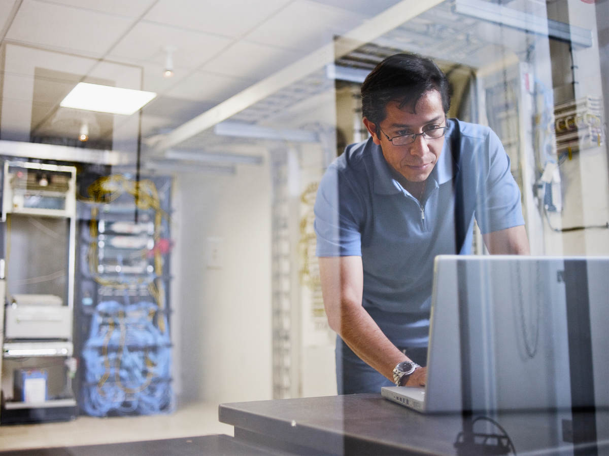 Man using a laptop with an IT server in the background