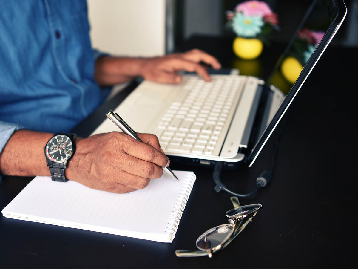 Close-up of a man’s hands, ready to take notes while following training on his laptop