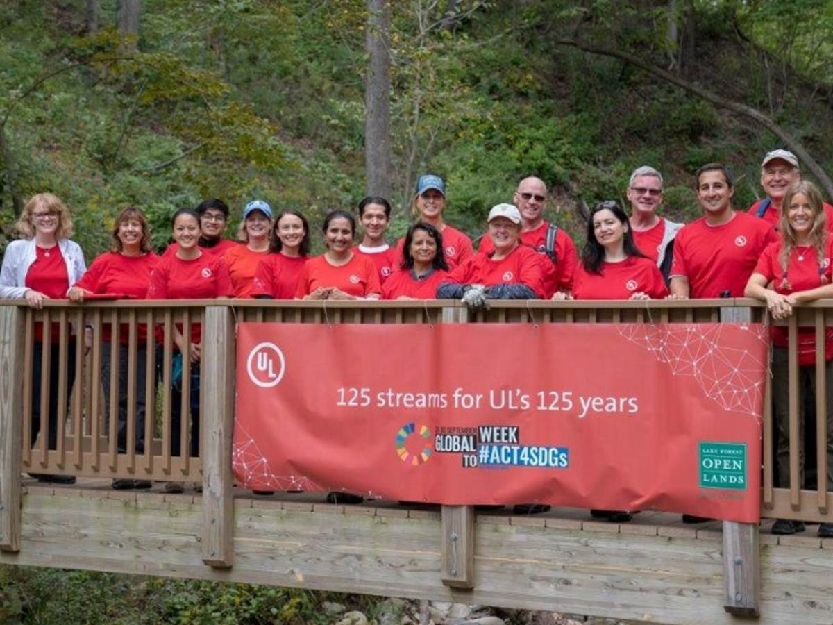 UL employees proudly pose on a wooden bridge on which has been hung a banner announcing 125 streams for 125 years.