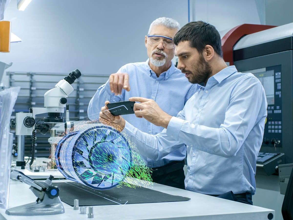 Two Engineers Works with Mobile Phone Using Augmented Reality Holographic Projection 3D Model of the Engine Turbine Prototype