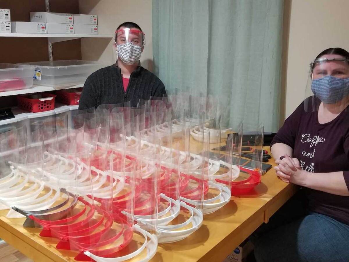 Ed and Brandi Miller sit on either side of a table filled with red and white face shields