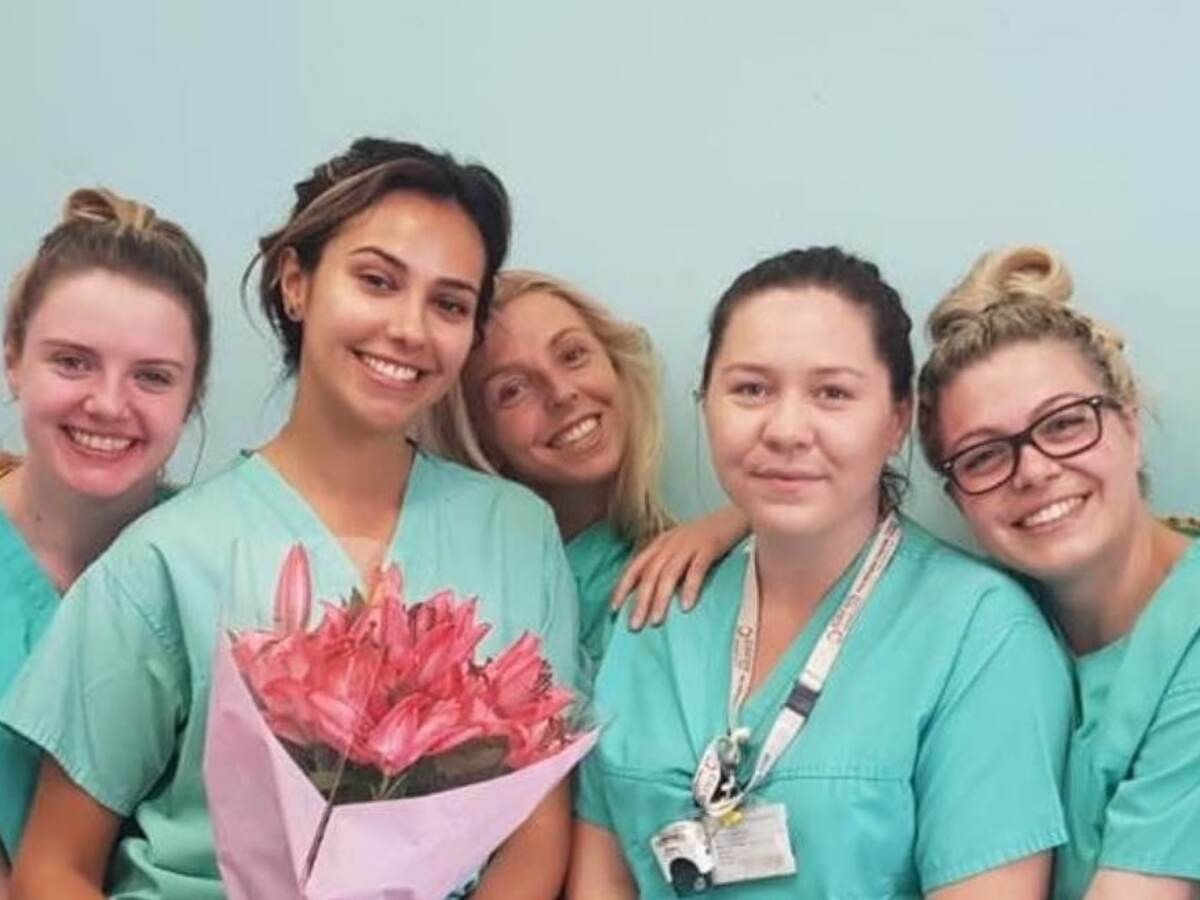 Five nurses wearing green scrubs, one who is holding a bouquet of flowers, pose for a picture. 