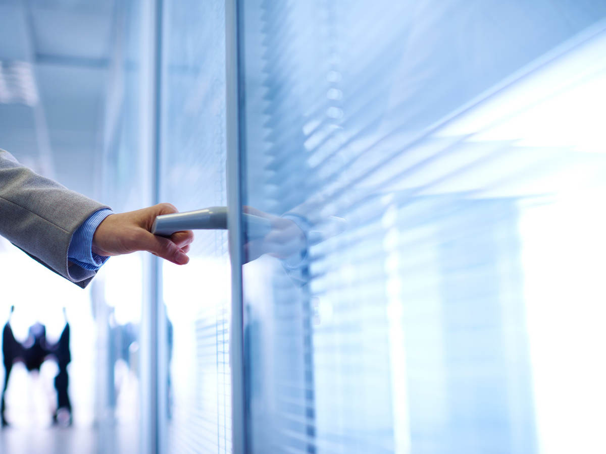 photo of a hand opening an office door, with people in background.